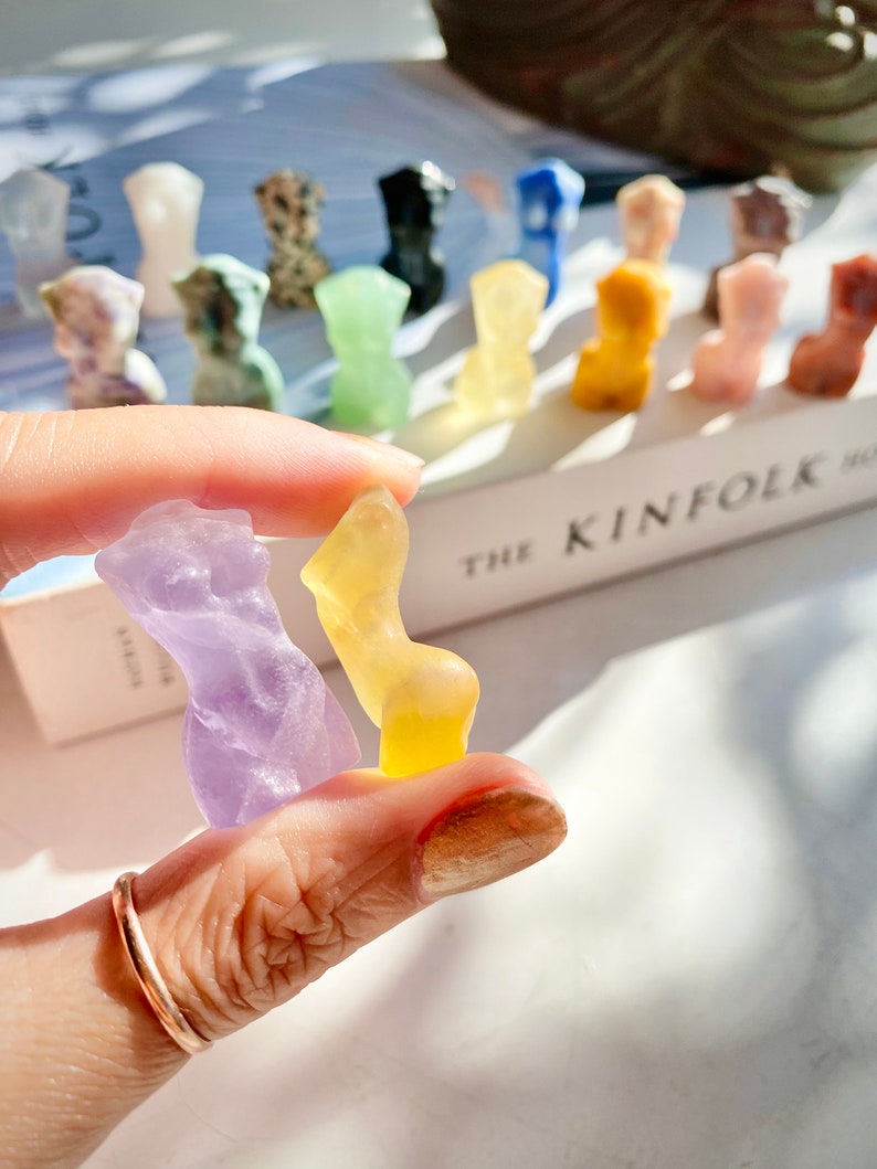 May include: Two small, hand-carved figurines made of translucent stone. The figurine on the left is purple and the figurine on the right is yellow.