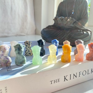 May include: A row of small, colourful, carved stone figurines of the human form, arranged on a book titled "The Kinfolk".