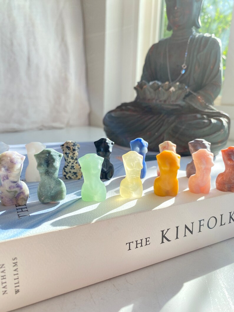 May include: A row of small, colourful, carved stone figurines of the human form, arranged on a book titled "The Kinfolk".