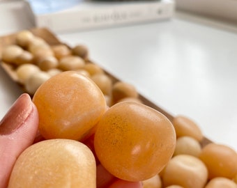 May include: A collection of smooth, polished, light orange carnelian stones. The stones are tumbled and have a natural, earthy look.