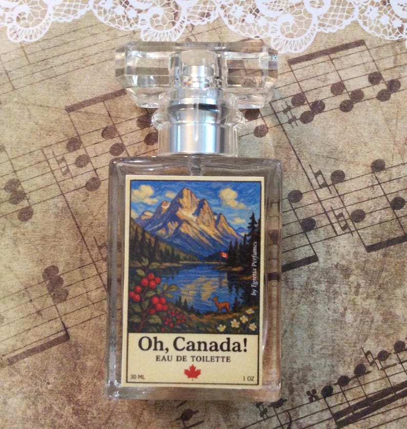 May include: A clear glass perfume bottle with a rectangular label featuring a mountain landscape scene. The label reads "Oh, Canada!" and "Eau de Toilette." The bottle has a silver collar and a clear, faceted cap. The bottle contains 1 oz of perfume.