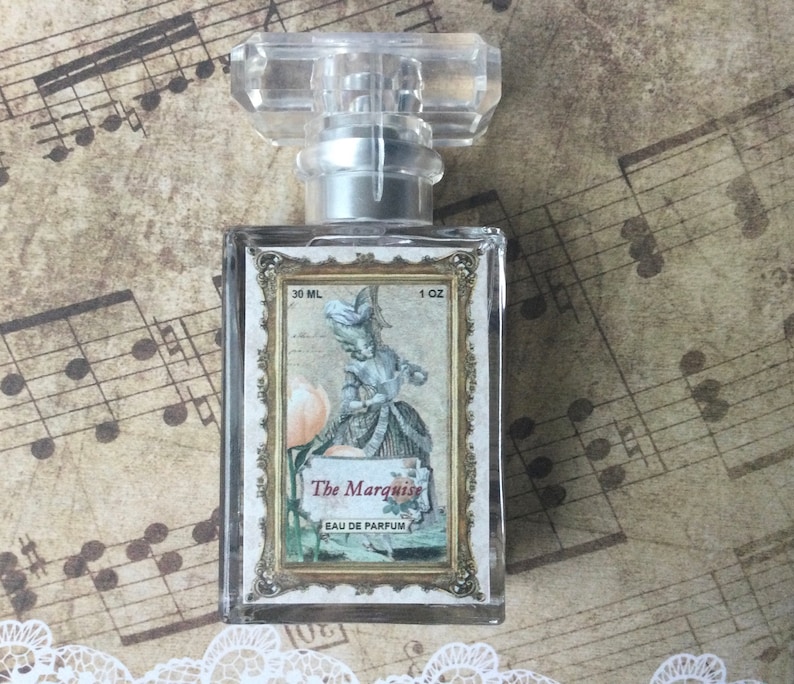 May include: A clear glass bottle of perfume with a gold label. The label features a vintage illustration of a woman in a dress and the text "The Marquise Eau de Parfum". The bottle is 1 oz (30 ml).
