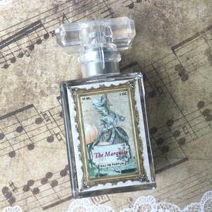 May include: A clear glass bottle of perfume with a gold cap and label. The label features a vintage illustration of a woman in a white dress and the text "The Marquise Eau de Parfum". The bottle is 30 ml or 1 oz.
