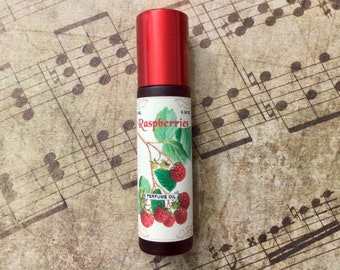 Pode incluir: Um frasco vermelho de roll-on com um rótulo branco que mostra um desenho de framboesas e o texto "Raspberries Perfume Oil 0.34 fl oz".