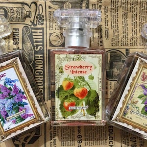 May include: Three perfume bottles with clear, faceted stoppers and decorative labels. The labels feature floral and fruit illustrations, including lilacs, strawberries, and violets. Each bottle contains 30 ml of Eau de Toilette.