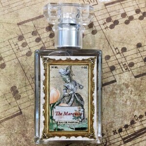 May include: A clear glass bottle of perfume with a gold-colored label. The label features a vintage illustration of a woman in a dress and the text "The Marquise Eau de Parfum". The bottle is 30 ml or 1 oz.