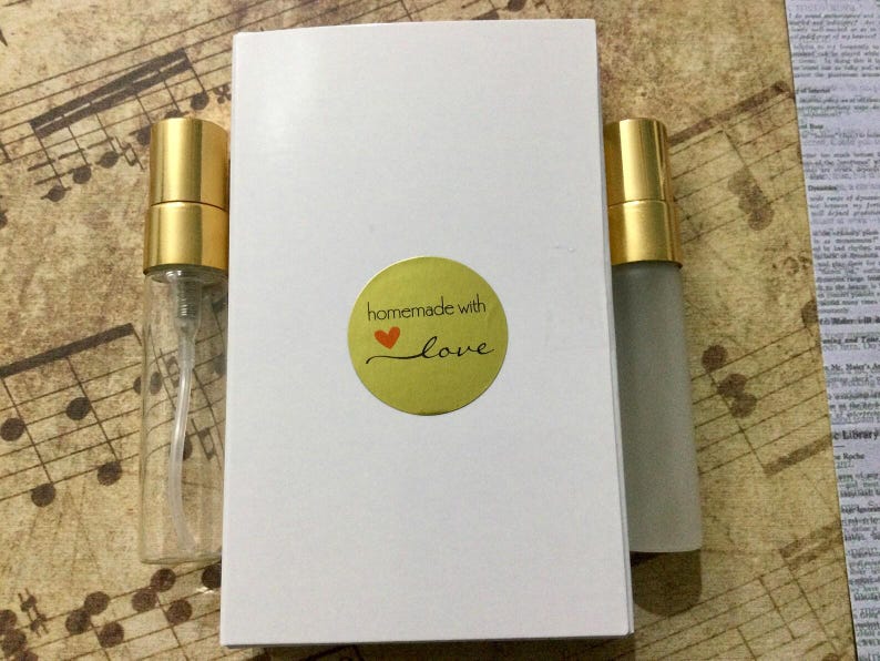 May include: A white box with a round sticker that reads "homemade with love" and a red heart. Two small perfume bottles with gold caps are next to the box. One bottle is clear, and the other is frosted.