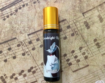 May include: A black roll-on bottle with a gold cap and a label that says "Goodnight Kiss" and "Perfume Oil". The label features a black and white illustration of a woman with a butterfly.