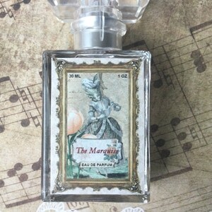 May include: A clear glass bottle of perfume with a gold-trimmed label. The label features a vintage illustration of a woman in a dress and the text "The Marquise Eau de Parfum 30 ML 1 OZ".