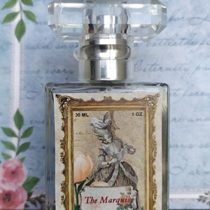 May include: A clear glass bottle of perfume with a gold-trimmed label. The label features a woman in a vintage dress and the text "The Marquise Eau de Parfum". The bottle is 30 ml or 1 oz.