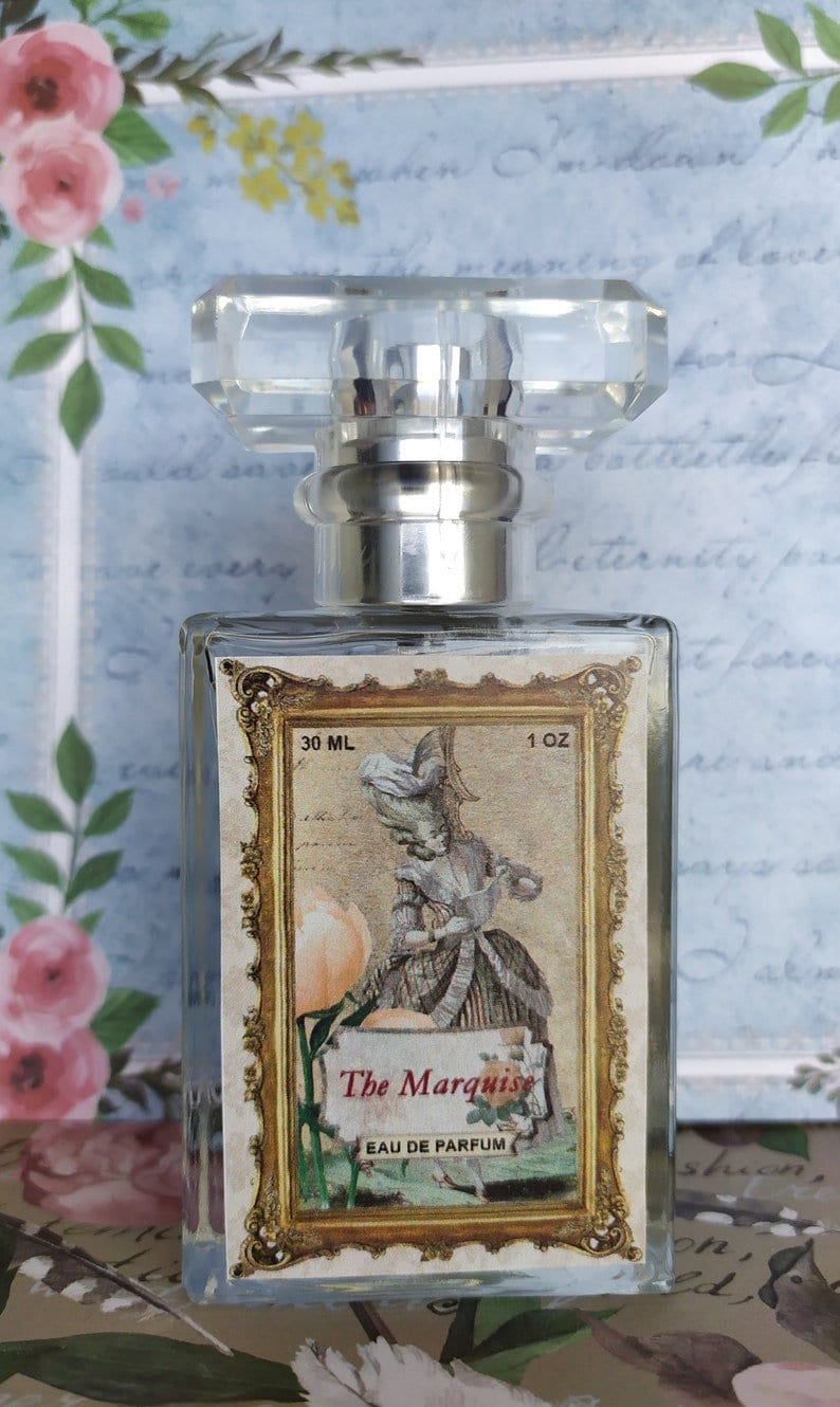 May include: A clear glass bottle of perfume with a gold-trimmed label. The label features a woman in a vintage dress and the text "The Marquise Eau de Parfum". The bottle is 30 ml or 1 oz.