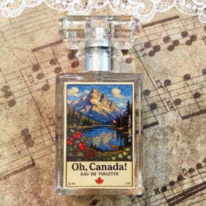 May include: A clear glass perfume bottle with a rectangular shape and a faceted crystal stopper. The label features a landscape painting of mountains, a lake, and a deer, with the text "Oh, Canada!" and "Eau de Toilette". The bottle contains 1 oz of perfume.