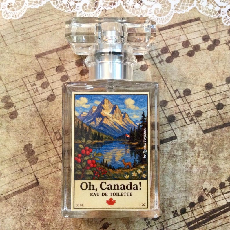 May include: A clear glass perfume bottle with a rectangular shape and a faceted crystal stopper. The label features a landscape painting of mountains, a lake, and a deer, with the text "Oh, Canada!" and "Eau de Toilette". The bottle contains 1 oz of perfume.