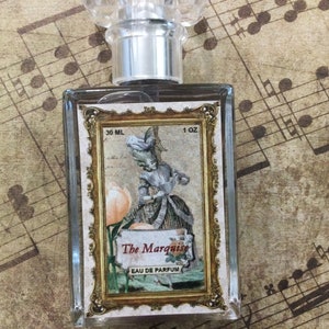 May include: A clear glass bottle of perfume with a gold-framed label. The label features a vintage illustration of a woman in a dress and the text "The Marquise Eau de Parfum 30 ML 1 OZ".