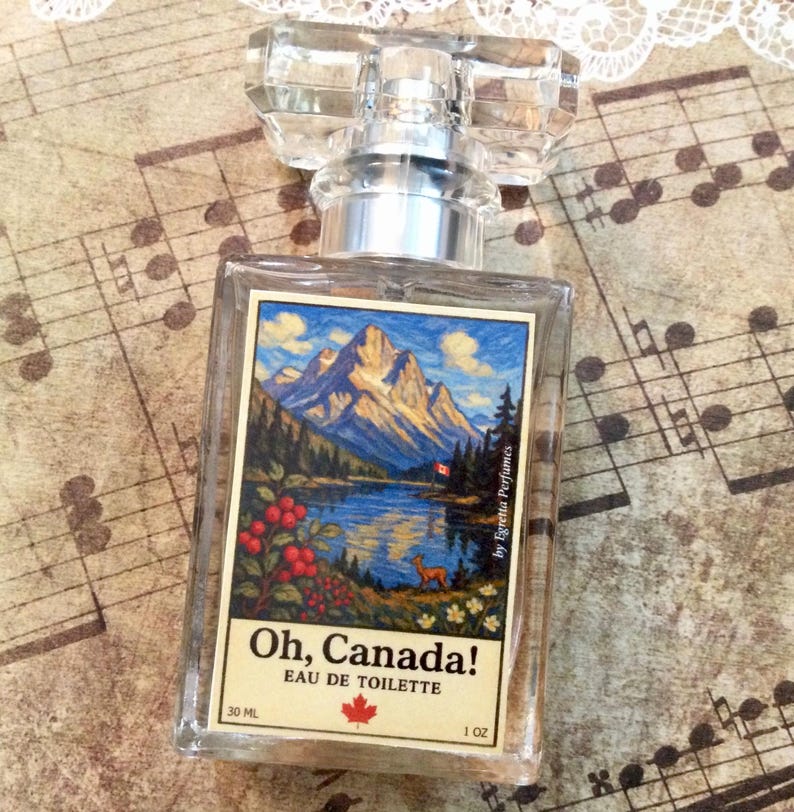 May include: A clear glass perfume bottle with a rectangular label featuring a mountain landscape scene. The label reads "Oh, Canada! Eau de Toilette" with a maple leaf. The bottle contains 1 oz of perfume.