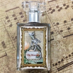 May include: A clear glass bottle of perfume with a silver cap. The bottle has a label with a gold frame and an illustration of a woman in a dress. The label reads "The Marquise Eau de Parfum" and "30 ML 1 OZ".