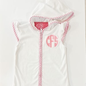 May include: White hooded towel robe with pink striped trim and a pink monogram "CFS" on the front.