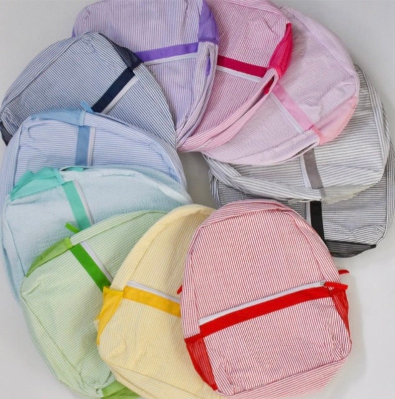 May include: A collection of seersucker backpacks in various colors, including blue, pink, yellow, and green. Each backpack features a striped pattern, a zippered front pocket, and a contrasting strap.