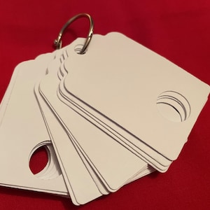 May include: A stack of white blank tags with a hole in the centre, attached to a silver ring.