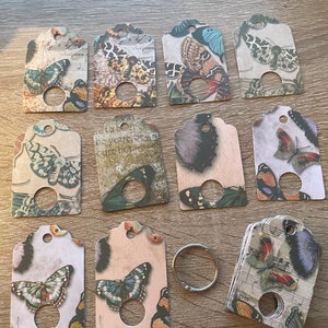 May include: A set of 10 butterfly-themed gift tags with a hole punched in the top. The tags are printed on a variety of papers with different patterns and colors. The butterflies are all different colors and sizes. There is also a silver key ring included.