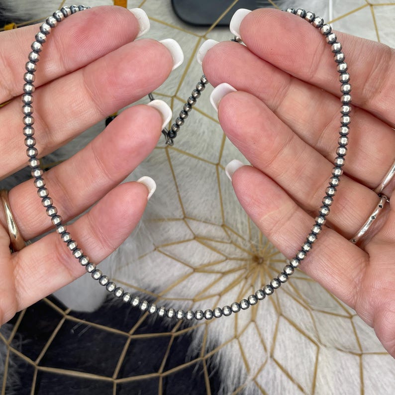 Peut inclure: Un bracelet d&eacute;licat en argent perl&eacute;. Le bracelet est compos&eacute; de petites perles rondes en argent enfil&eacute;es ensemble. Le bracelet est tenu par les mains d'une personne, mettant en valeur le bijou sur un fond neutre.