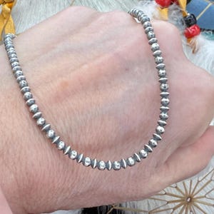 May include: A silver necklace with small, round beads. The beads have a textured surface and are evenly spaced.