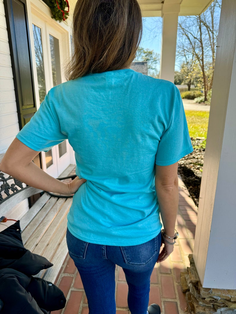 May include: A woman wearing a light blue t-shirt and blue jeans. The t-shirt is a simple design with no visible graphics or text.