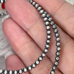 Peut inclure: Gros plan sur un rang de petites perles rondes de couleur argent&eacute;e. Les perles sont enfil&eacute;es ensemble, formant un collier ou un bracelet. Les perles ont un &eacute;clat m&eacute;tallique et sont espac&eacute;es uniform&eacute;ment.