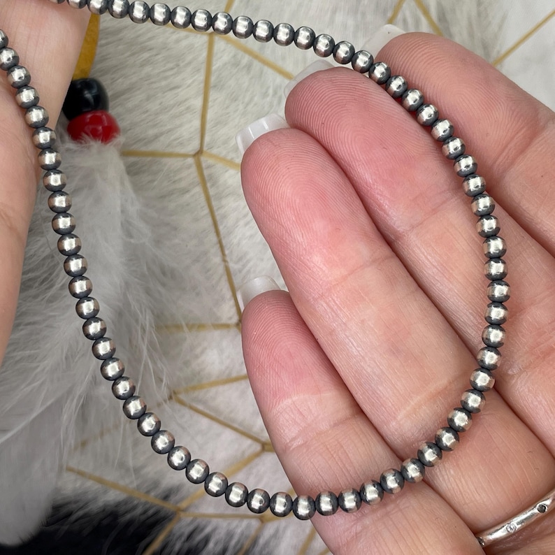 Peut inclure: Un d&eacute;licat collier de perles argent&eacute;es. Le collier est compos&eacute; de petites perles rondes argent&eacute;es enfil&eacute;es ensemble. Les perles ont un aspect l&eacute;g&egrave;rement facett&eacute;, captant la lumi&egrave;re. Le collier est pr&eacute;sent&eacute; sur un fond doux et neutre.