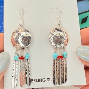 May include: Silver earrings with a circular design, turquoise and red beads, and feather pendants. The earrings are stamped with a floral pattern and have a hook closure. The text "STERLING SIL" is visible.