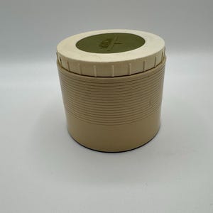 May include: A vintage beige thermos with a cream lid and a green central disc. The thermos has horizontal ridges around the body, and the word "Thermos" is visible on the lid.
