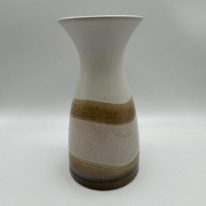 May include: A ceramic vase with a white top and a body featuring horizontal bands of brown and beige. The vase has a flared opening and a rounded base, suitable for displaying flowers or as a decorative piece.