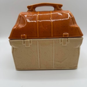 Op de afbeelding: Een tweekleurige keramische lunchbox met een handvat. De bovenkant is een gespikkeld oranjebruin en de onderkant een gespikkeld beige. De lunchbox heeft een rechthoekige vorm met een deksel dat goed past. De handgreep is gebogen en in het deksel geïntegreerd.