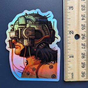 以下が含まれることがあります： ワイヤーとチューブが付いた未来的なヘルメットをかぶった人のホログラフィックステッカー。その人は長い黒髪とあごひげを生やしています。ステッカーの高さは約6.5cmです。