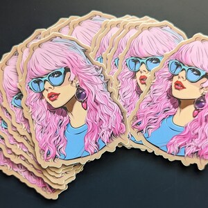May include: A stack of stickers featuring a cartoon illustration of a woman with pink hair, blue sunglasses, and a blue shirt. The woman is wearing large, purple earrings.
