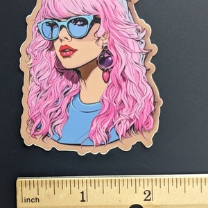 May include: A sticker featuring a cartoon illustration of a woman with pink hair, blue sunglasses, and a blue shirt. She is wearing a large, dangling earring with a purple stone.