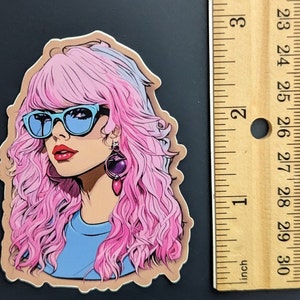 May include: A sticker featuring a woman with pink and purple hair, wearing blue sunglasses and a blue shirt. She has a purple and pink earring.