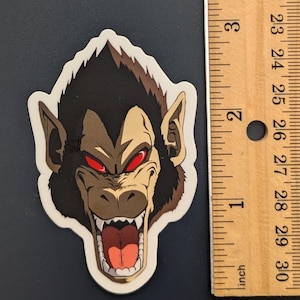 May include: A sticker featuring a close-up of a snarling, brown and black ape with red eyes. The ape's mouth is open, revealing sharp teeth and a pink tongue.