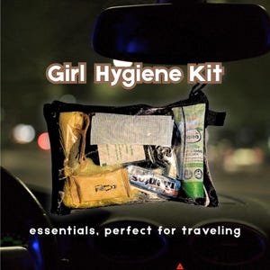 Op de afbeelding: Een zwart mesh reiskitje hangt aan de achteruitkijkspiegel van een auto. De kit bevat diverse hygiëneproducten, waaronder een lotion, tissues en andere benodigdheden. Tekst op de kit luidt "Girl Hygiene Kit" en "essentials, perfect for traveling."