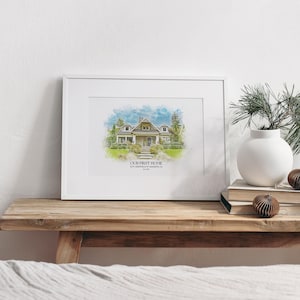 May include: A white framed print with a watercolor illustration of a house. The text "OUR FIRST HOME" is below the image, along with the address and date.