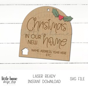 May include: A brown wooden Christmas ornament with the text "Christmas in our new home" and a small house icon. The ornament has a space for personalization with the text "Name, Address, Year Here ETC."