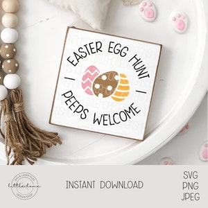 May include: A white wooden sign with the text "Easter Egg Hunt - Peeps Welcome" in black lettering. The sign features a pink and yellow egg design.