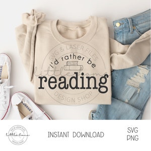 May include: A beige sweatshirt with the text "I'd rather be reading" in a black circle with a stack of books inside. The text "SVG & LASER FILES" and "DESIGN SHOP" are also in the circle. The sweatshirt is lying on a white surface with a pair of white trainers and a pair of blue jeans.