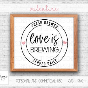 Op de afbeelding: Een zwart-wit grafisch ontwerp met een cirkel en de tekst "Fresh Brewed Love is Brewing Served Daily". De cirkel heeft twee roze harten aan weerszijden van de tekst. De grafiek is ingelijst in een bruin houten frame.