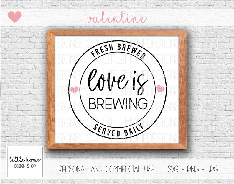 Op de afbeelding: Een zwart-wit grafisch ontwerp met een cirkel en de tekst "Fresh Brewed Love is Brewing Served Daily". De cirkel heeft twee roze harten aan weerszijden van de tekst. De grafiek is ingelijst in een bruin houten frame.