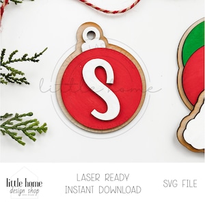 May include: Wooden Christmas ornament with a red center and a white letter "S". The ornament has a natural wood border and a loop for hanging. The text "LASER READY INSTANT DOWNLOAD" is visible.