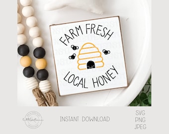 Puede incluir: Un letrero de madera blanco con texto negro que dice "Farm Fresh Local Honey". Un panal de abejas amarillo y negro con abejas está en el centro del letrero.