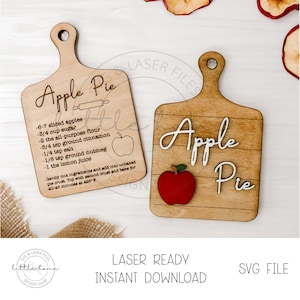 以下が含まれることがあります： 「Apple Pie」と書かれた木製のまな板が2枚。1枚はアップルパイの材料リストと小さな赤いリンゴのグラフィックが描かれている。もう1枚は大きな赤いリンゴのグラフィックが描かれている。
