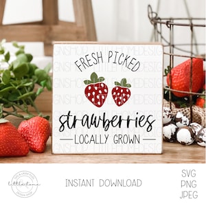 May include: A white wooden sign with the text "FRESH PICKED strawberries - LOCALLY GROWN -" and two red strawberries with white dots on a white background.