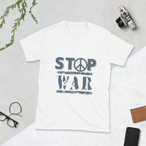 Könnte beinhalten: Weißes T-Shirt mit einem grauen Aufdruck, der "STOP WAR" mit einem Friedenssymbol sagt.